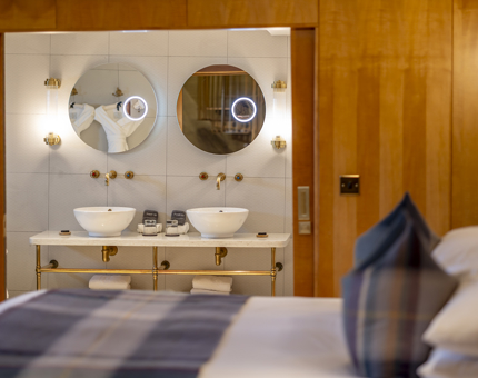 A cabin aboard Fingal Hotel. There is a view of the bed and behind that a bathroom with two round mirrors. 