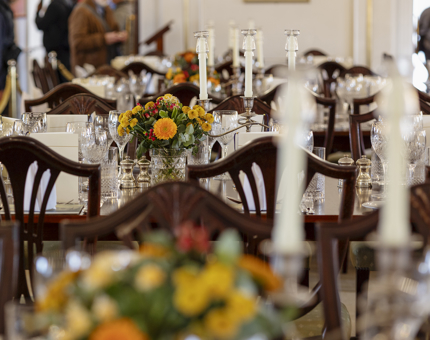 A close up of tables in the State Dining Room set for an evening event. They are decorated with autumnal coloured flowers. 