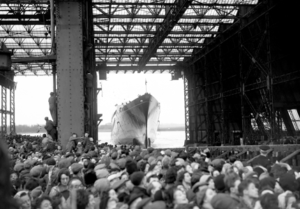 A black and white image of Britannia in dock, there are lots of people looking at it.