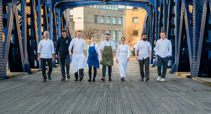 A group of chefs walking across a bridge in a line. 