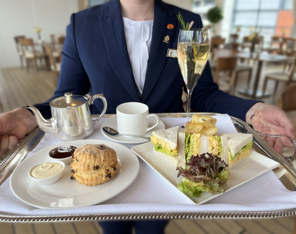 A Waiter holding a tray containing a cream tea in the Tea Room. 