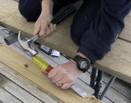 A close-up of a man hammering together planks of wood. 