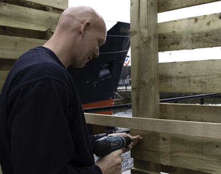 Man drills planks of wood in fence.