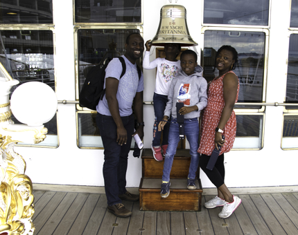 A family group of visitors pose next to Britannia's ship bell. 