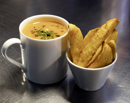 Mug of soup sits next to a bowl of potato wedges. 