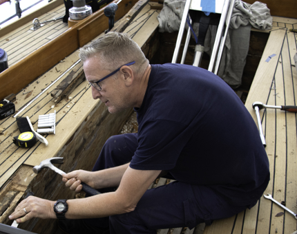 Maintenance man sitting hammers a part of the Royal Racing Yacht, Bloodhound.