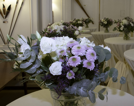 Close-up of a large vase of purple and cream flowers on a table with other table decorations in the background in the State Dining Room. 