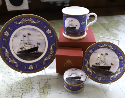 Royal Yacht Britannia souvenir plate, tankard and jewellery box are displayed sitting on a map of the world. 