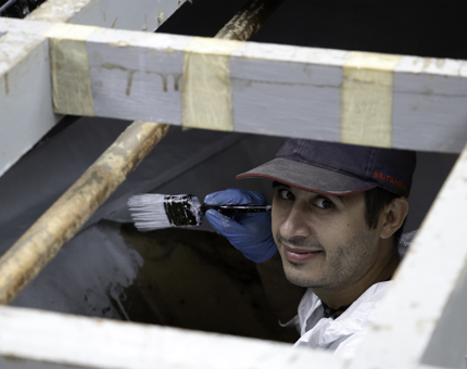 Man holding a paintbrush paints a part of the boat. 