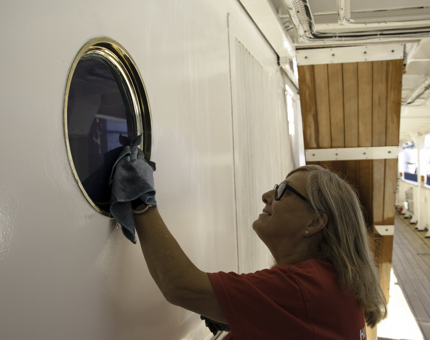 Housekeeper polishes a porthole.