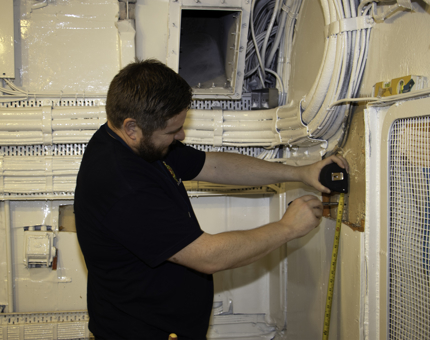 Man holds measuring tape against wall. 