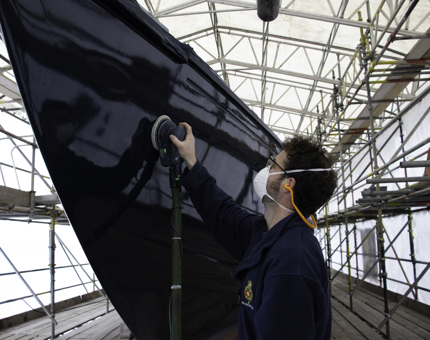 Man sands the side of Royal Racing Yacht Bloodhound. 