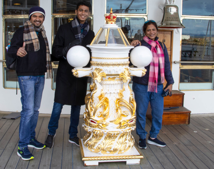 Family group of two men and one woman smile while standing next to Britannia's binnacle compass on deck. 
