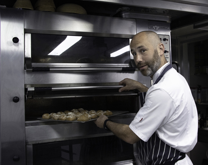 Chef removes a tray of freshly baked rolls from the oven. 