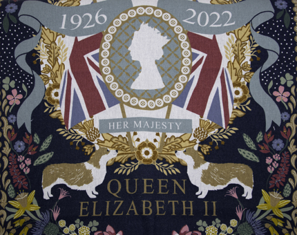 Commemorative tea towel celebrating the life of Queen Elizabeth II. A Union flag, corgis and a floral border appear on the tea towel design.