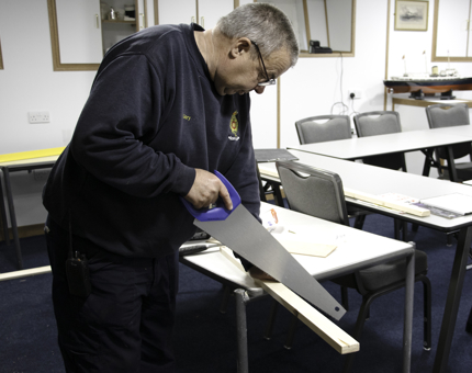 Maintenance team member saws a length of wood. 