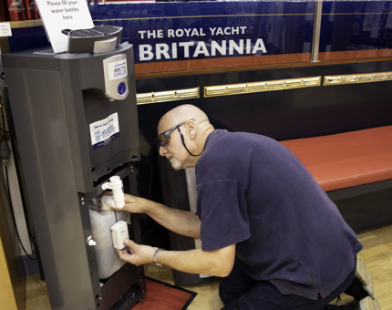 Man kneels down while inspecting a watercooler. 
