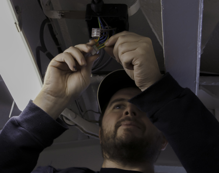 Maintenance team member holds wires while installing new lights in ceiling. 