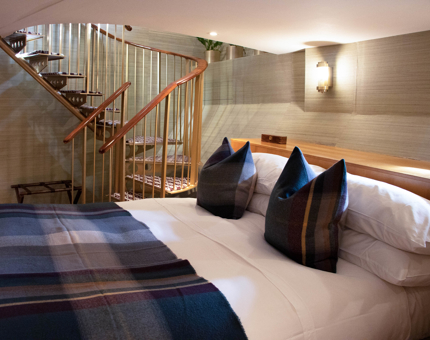 Lower bedroom level of Fingal duplex cabin shows bed with tartan covers and a spiral staircase. 