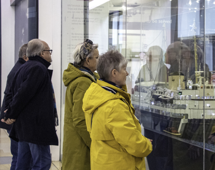 A small group of visitors look at a display case containing a large LEGO model of Britannia.