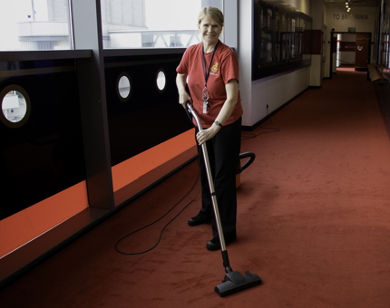 A Housekeeper is vacuuming the red carpet inside the Visitor Centre.
