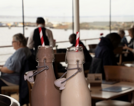 Two milkshakes in glass bottles with stripey straws. 