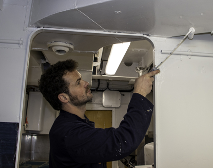 A man uses a paint roller to paint the Training Room Galley. 