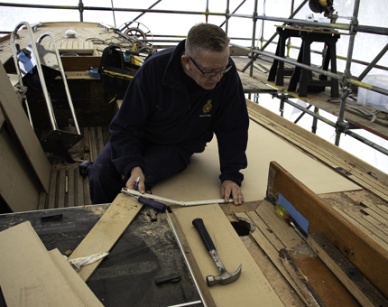 Maintenance team member measures up plywood to replace parts of the deck.