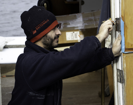 Maintenance man fits new hinges to a door on Britannia.