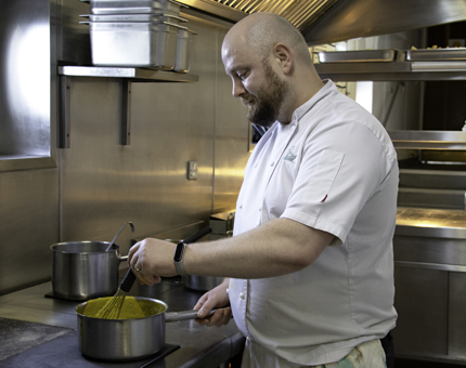 Chef stirs sauce in a pan within the Galley. 