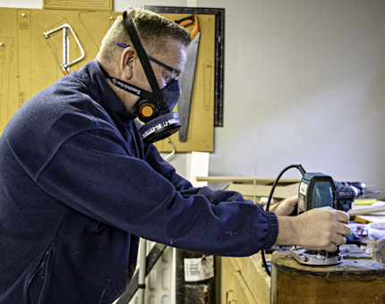 Maintenance team member holds a router to repair a winch block from Royal Racing Yacht Bloodhound.