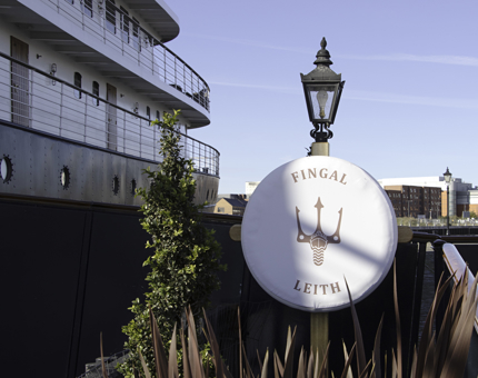 Outside view of Fingal with cabins, portholes, and lampost displaying Fingal's logo.