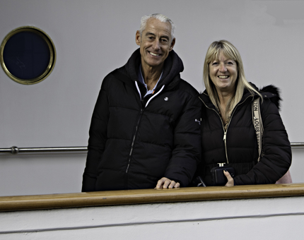Two visitors smiling next to a handrail on an outside deck. 