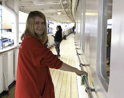 A Housekeeper wearing a red fleece jacket polishing hand railings. 