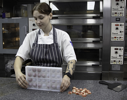 A Pastry Chef removes pink and white chocolates from a mould in the Galley. 