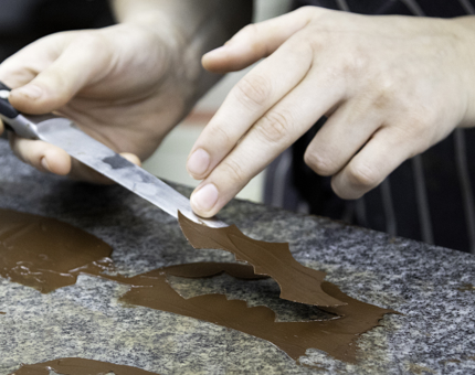 A close-up view as a Chef carefully cuts out bat wings shapes from chocolate. 