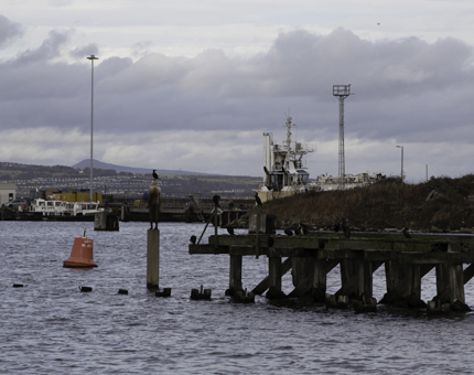 A life-size statue of a person at the end of an old pier. 