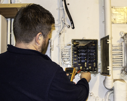 A member of the Maintenance team inspects a fuse box. 