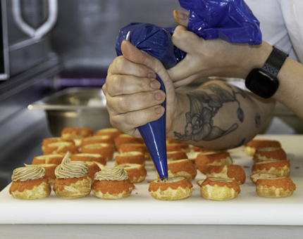 A Chef is piping mixture into a tray of choux buns for Afternoon Tea. 