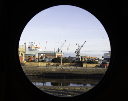 The view of the Port of Leith with cranes on the skyline through a porthole. 