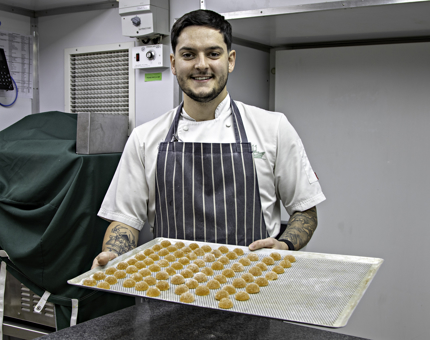A Chef holds a tray up filled with dessert treats. 