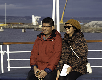 Smiling man and woman sit on bench on Britannia's outdoor Verandah Deck. 
