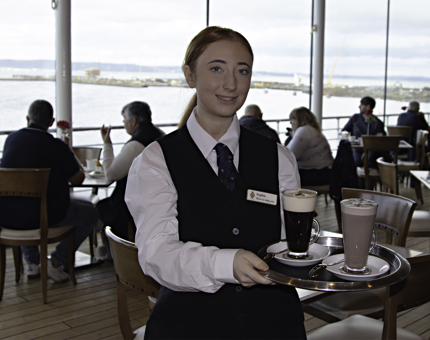 Waiter carries a tray containing tall glasses of a hot chocolate and coffee in the Tea Room. 