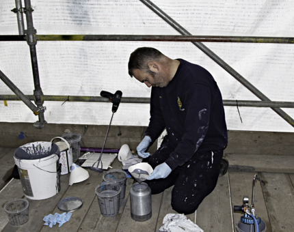Man pours paint into container in preparation to spray paint.