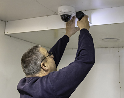 Maintenance man holds a powertool as he fits a panel into the ceiling.