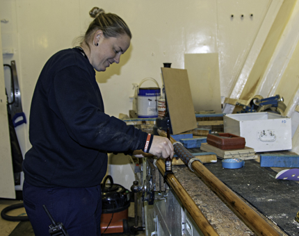 Maintenance woman uses a paintbrush to varnish the boathooks. 