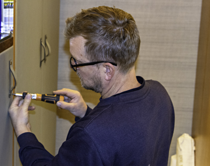 Maintenance man fixes a handle on a minibar door with a screwdriver in a Fingal cabin. 
