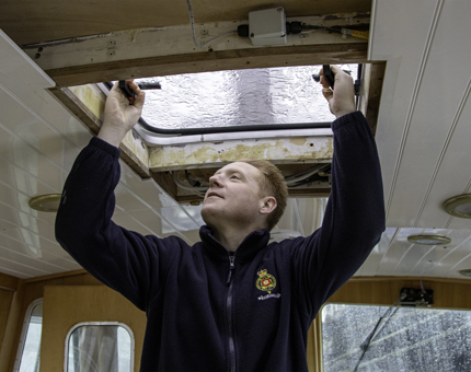 Man inspects a ceiling hatch is watertight on board Royal Nore.
