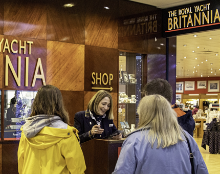Visitor Assistant woman greeting two women at the Welcome Podium at Britannia's Visitor Centre. 
