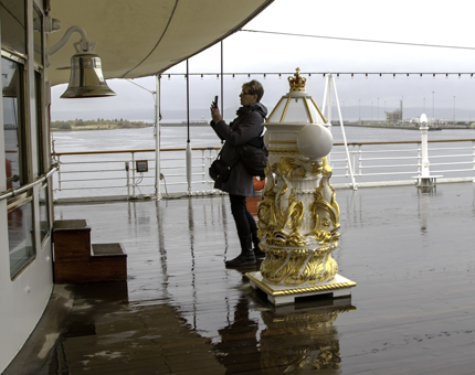 A rainy day outside on Britannia's Verandah Deck where a woman takes a photograph of the Bell. 
